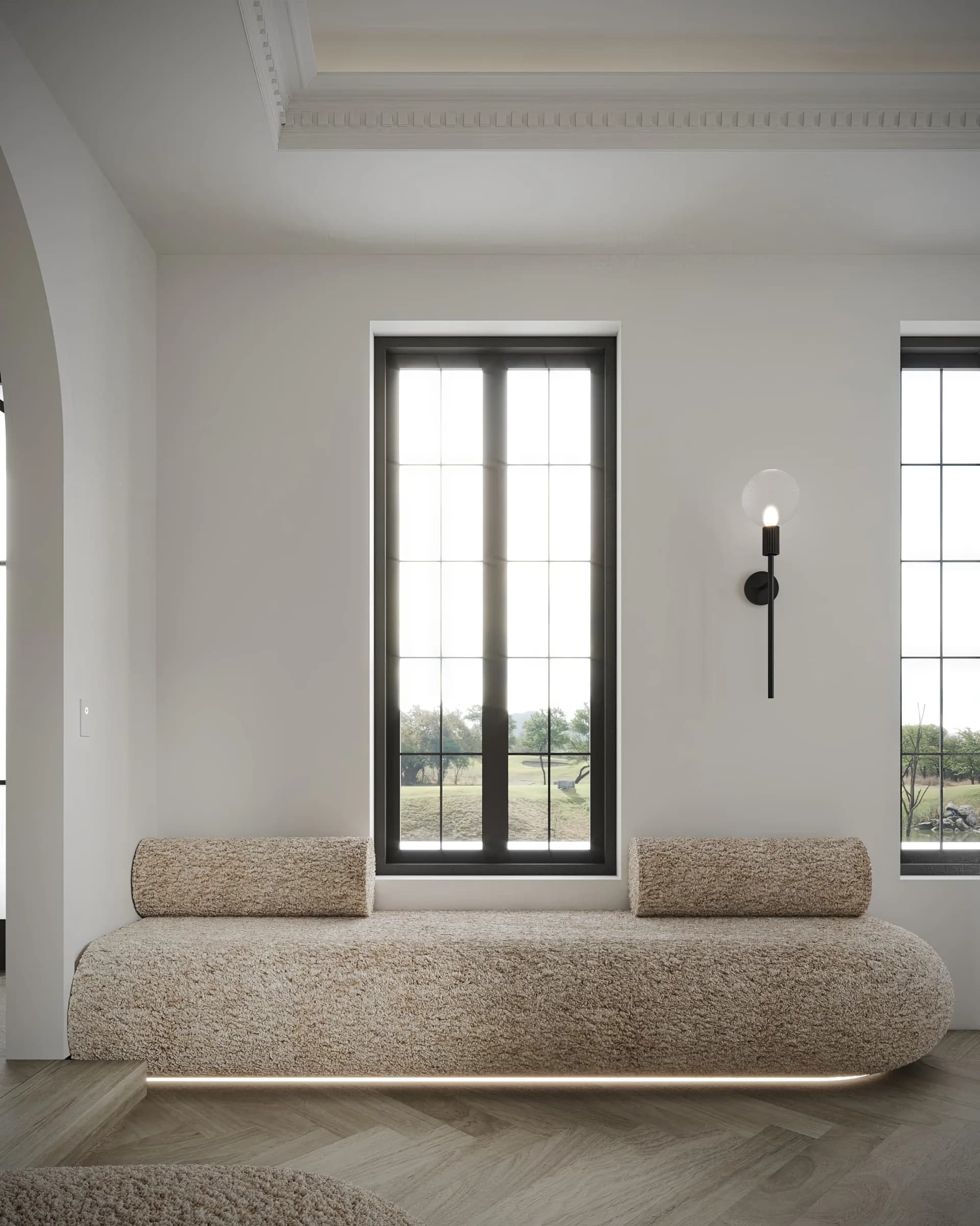 Sitting nook with a bouclé window seat beneath black-framed glazing, a slender sconce and ornate ceiling cornice