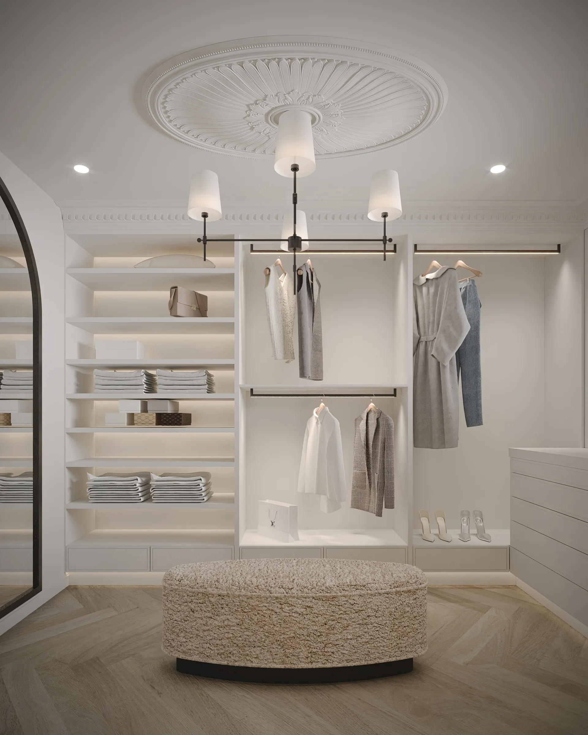 Walk-in wardrobe with illuminated white joinery, a bouclé ottoman and chandelier set into an ornate ceiling rose