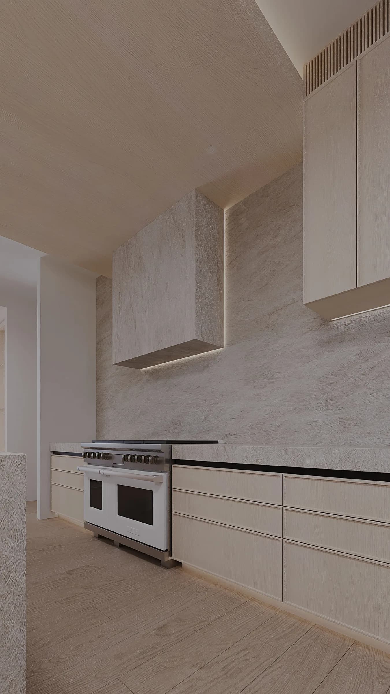 Pale timber kitchen cabinetry frames a white range, textured stone splashback and monolithic illuminated hood