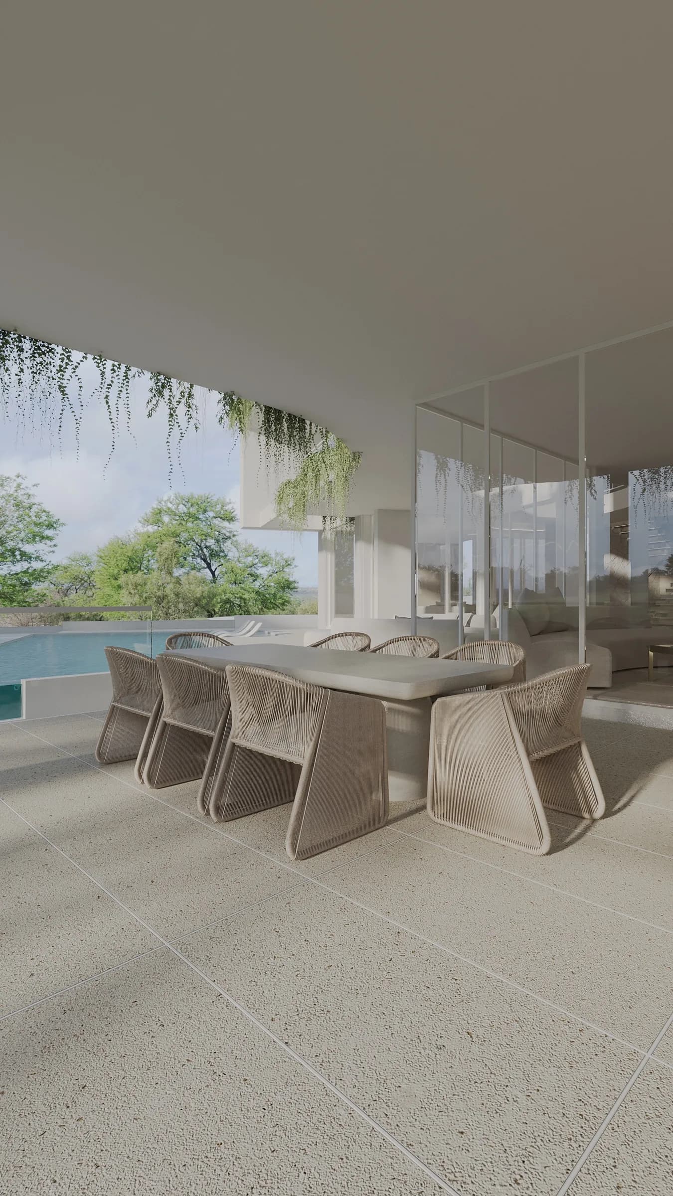 Covered terrace with a solid stone dining table, woven rope chairs, hanging greenery and the pool beyond