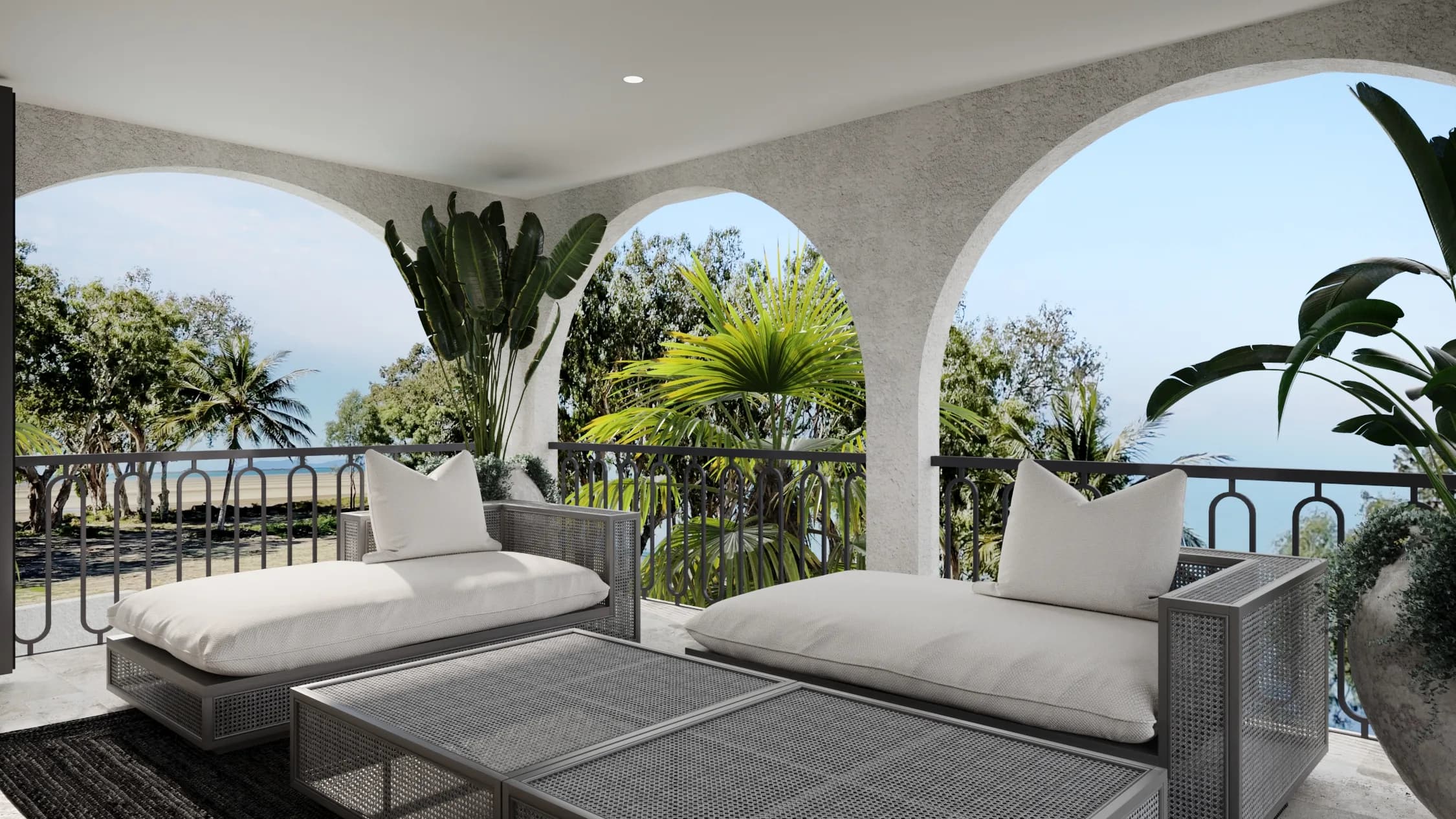 Covered balcony lounge with woven grey daybeds beneath broad stucco arches, framed by palms and a coastal view