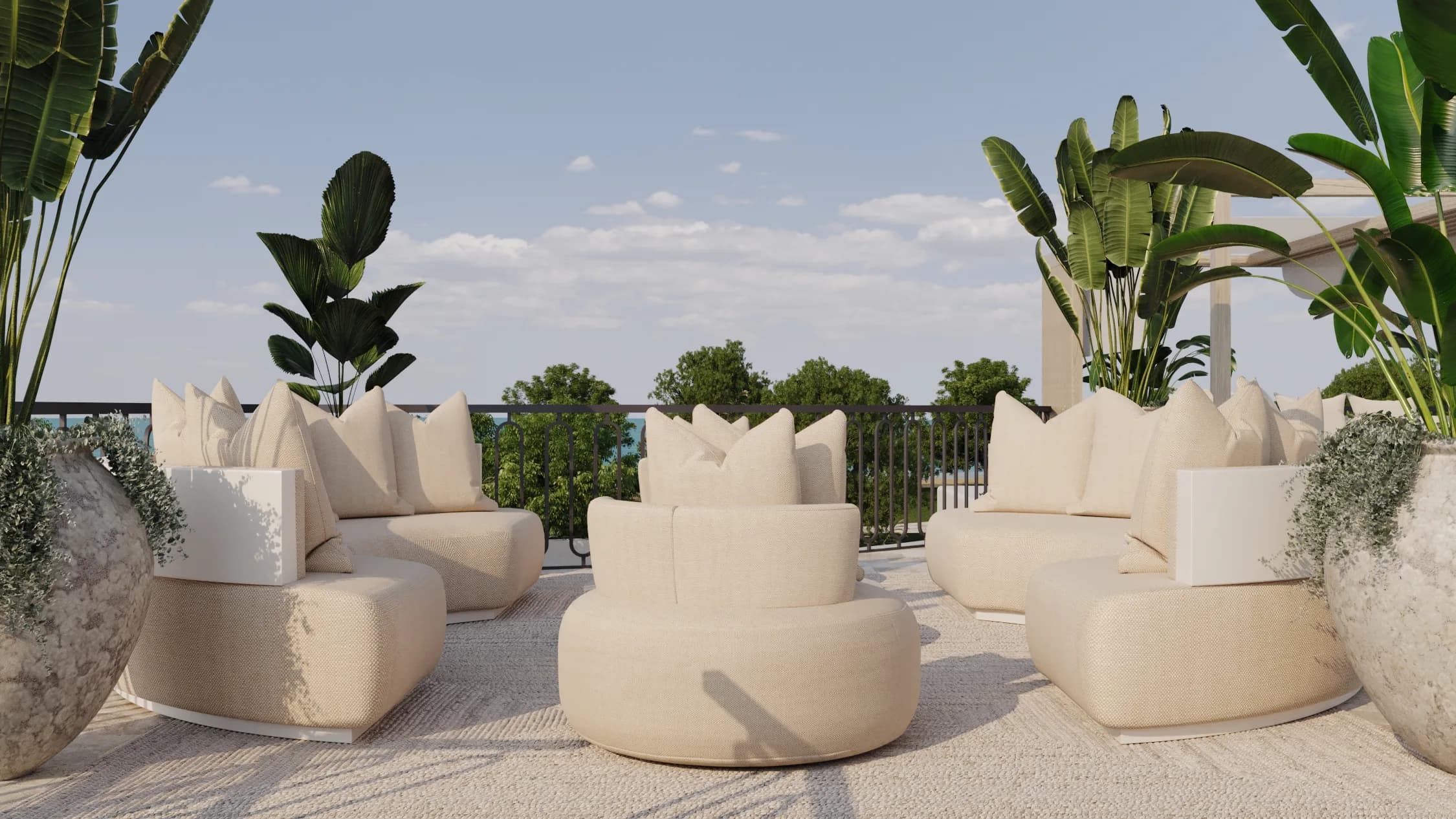 Curved cream armchairs gather on a woven rug between tropical planters and black iron railing beneath open sky