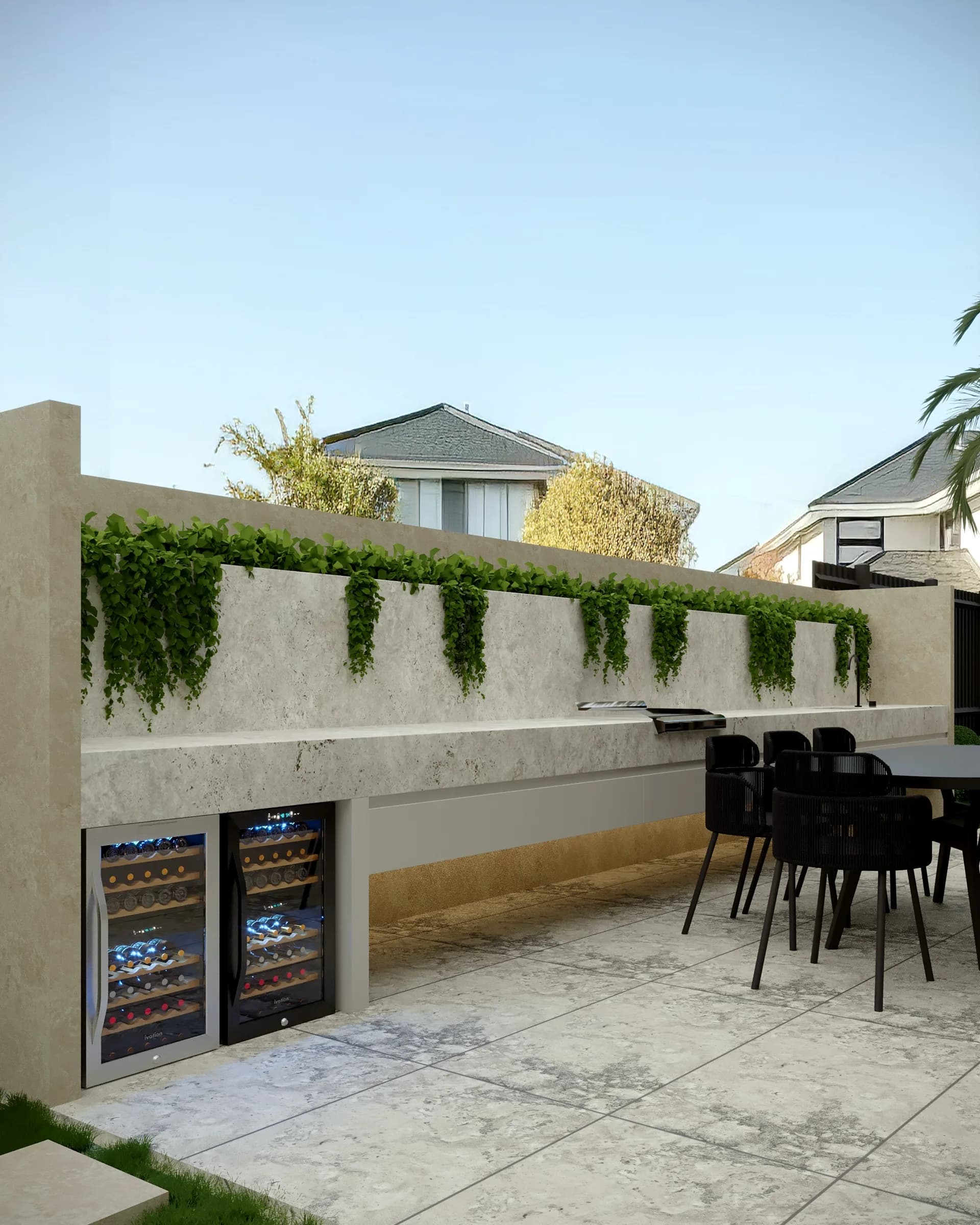 Outdoor kitchen with a long pale stone counter, twin wine fridges, black chairs and cascading greenery
